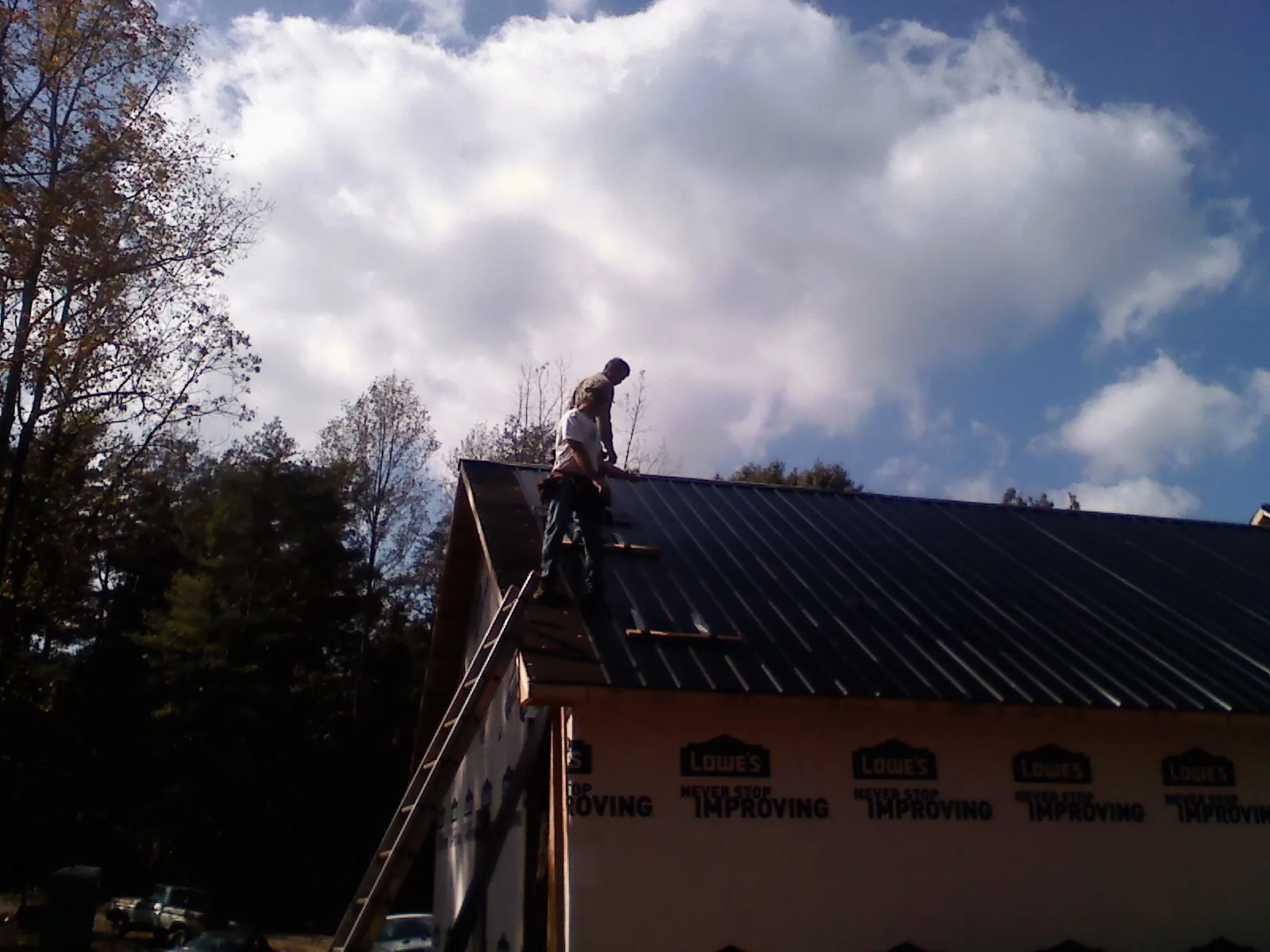 Roofer fastening dark metal panels high against a cloudy sky, from a Roof Inspection job in Homer